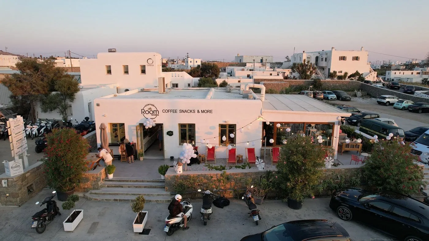 Το κατάστημα από ψηλά την ώρα του ηλιοβασιλέματος, με τις κόκκινες πολυθρόνες στη βεράντα και τα αυτοκίνητα παρκαρισμένα δίπλα στον δρόμο.