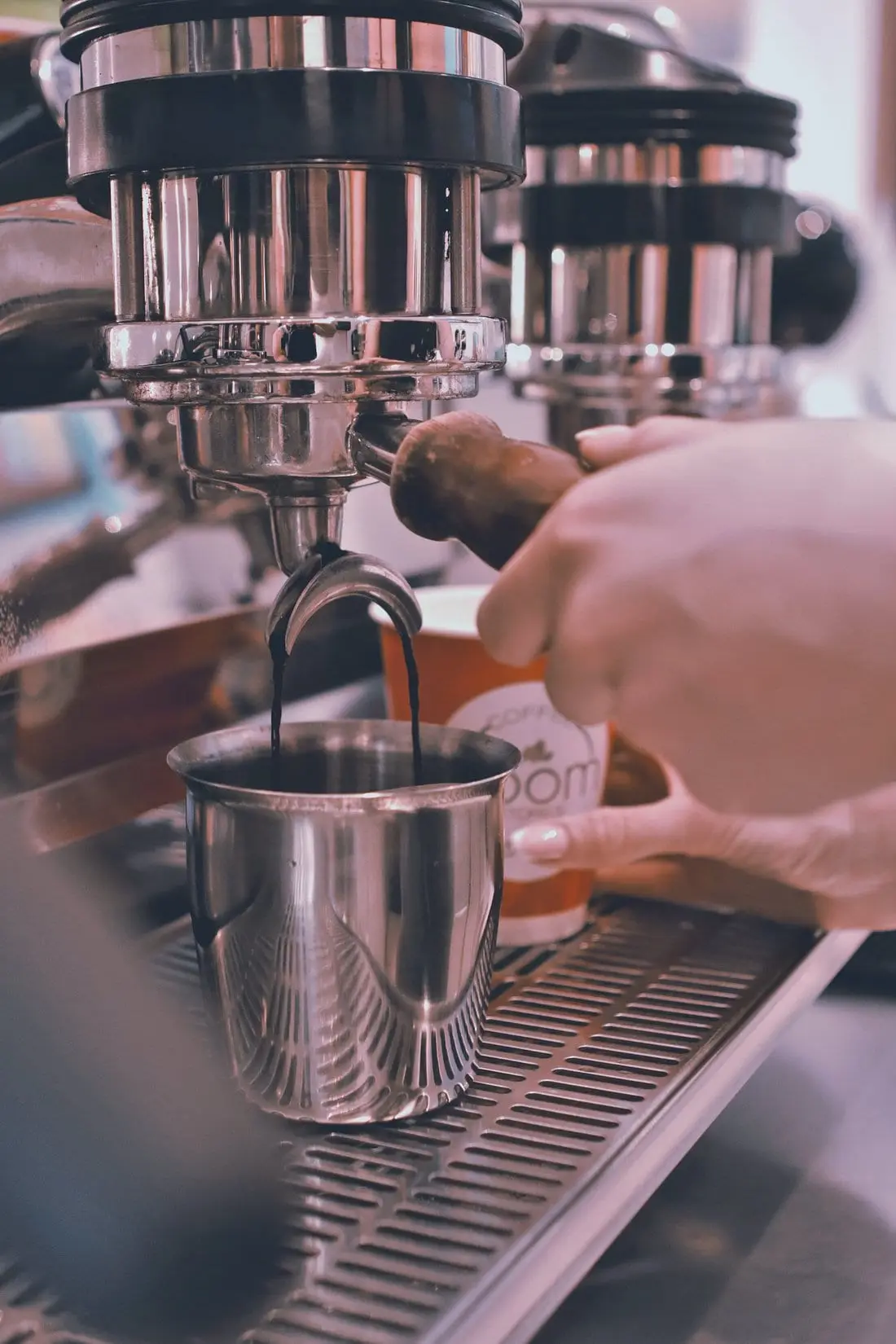 Espresso τρέχει από τη μηχανή σε ανοξείδωτο σκεύος, με το χέρι της barista στο φίλτρο.